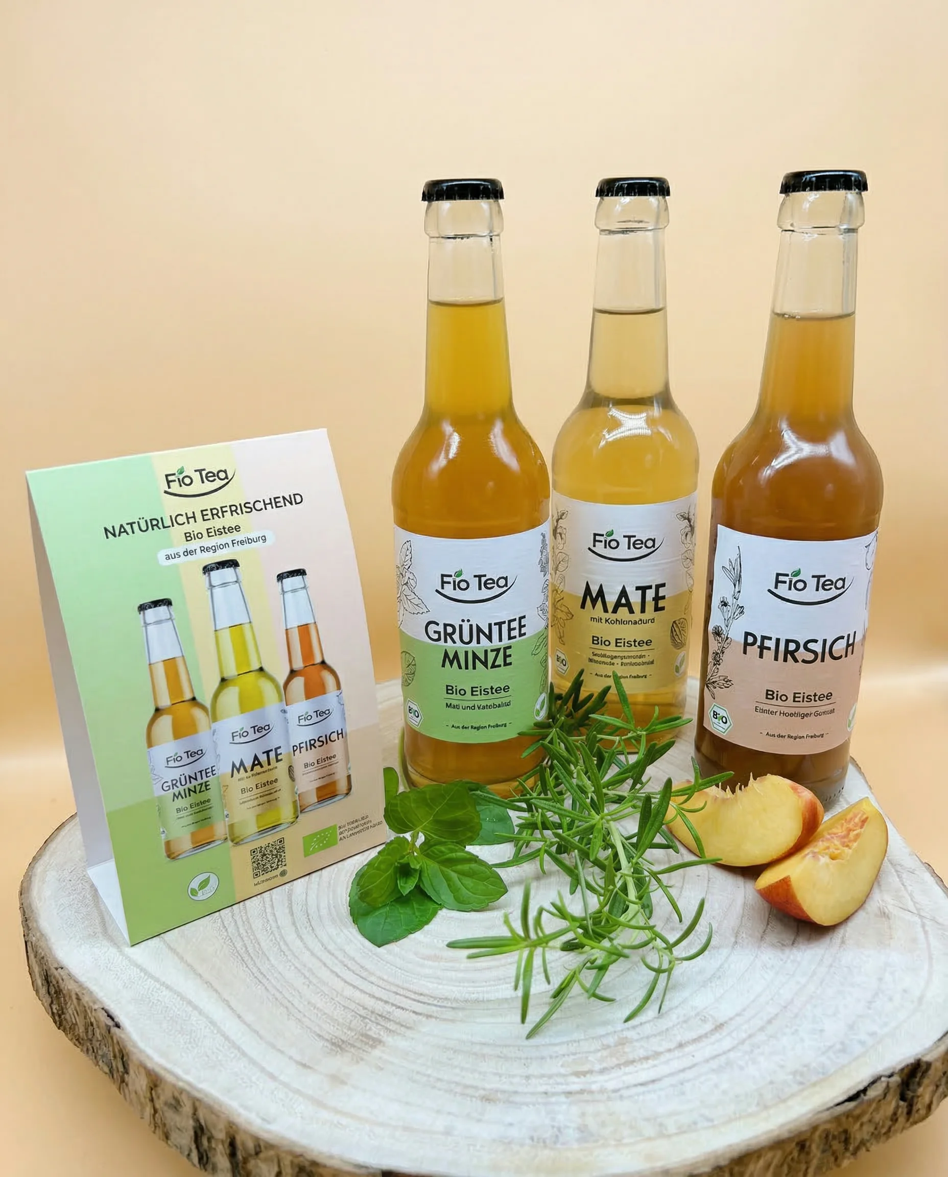 Fio Tea Bio Eistee Sortiment — alle drei Sorten mit Marketingmaterial auf einer Holzscheibe